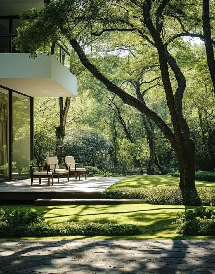 A villa terrace with lounge chairs facing a lawn under mature trees